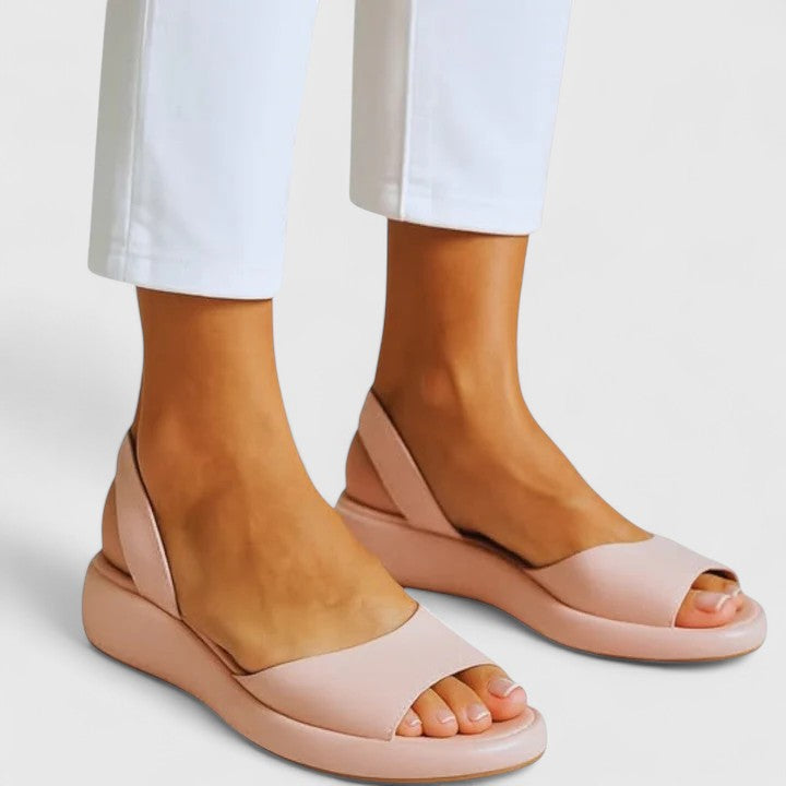 Roze Emrynn orthopedische sandalen gedragen door een vrouw die voorover buigt om de sandalen te presenteren.