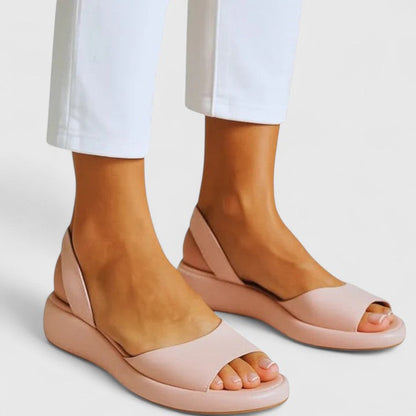 Roze Emrynn orthopedische sandalen gedragen door een vrouw die voorover buigt om de sandalen te presenteren.