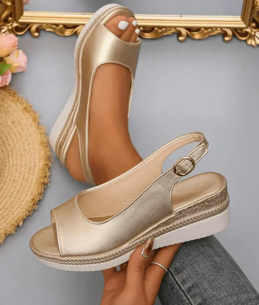 Model draagt gouden Ange sandalen in close-up, met focus op de bandjes en zool.