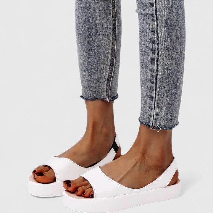Model met gele Emrynn sandalen wandelt op een effen ondergrond, toont de pasvorm en het comfort.